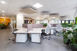 Bureau moderne à aire ouverte avec des bureaux blancs, des chaises ergonomiques, des panneaux de séparation, des plantes en pot et une lumière vive. Aucune personne n'est présente.