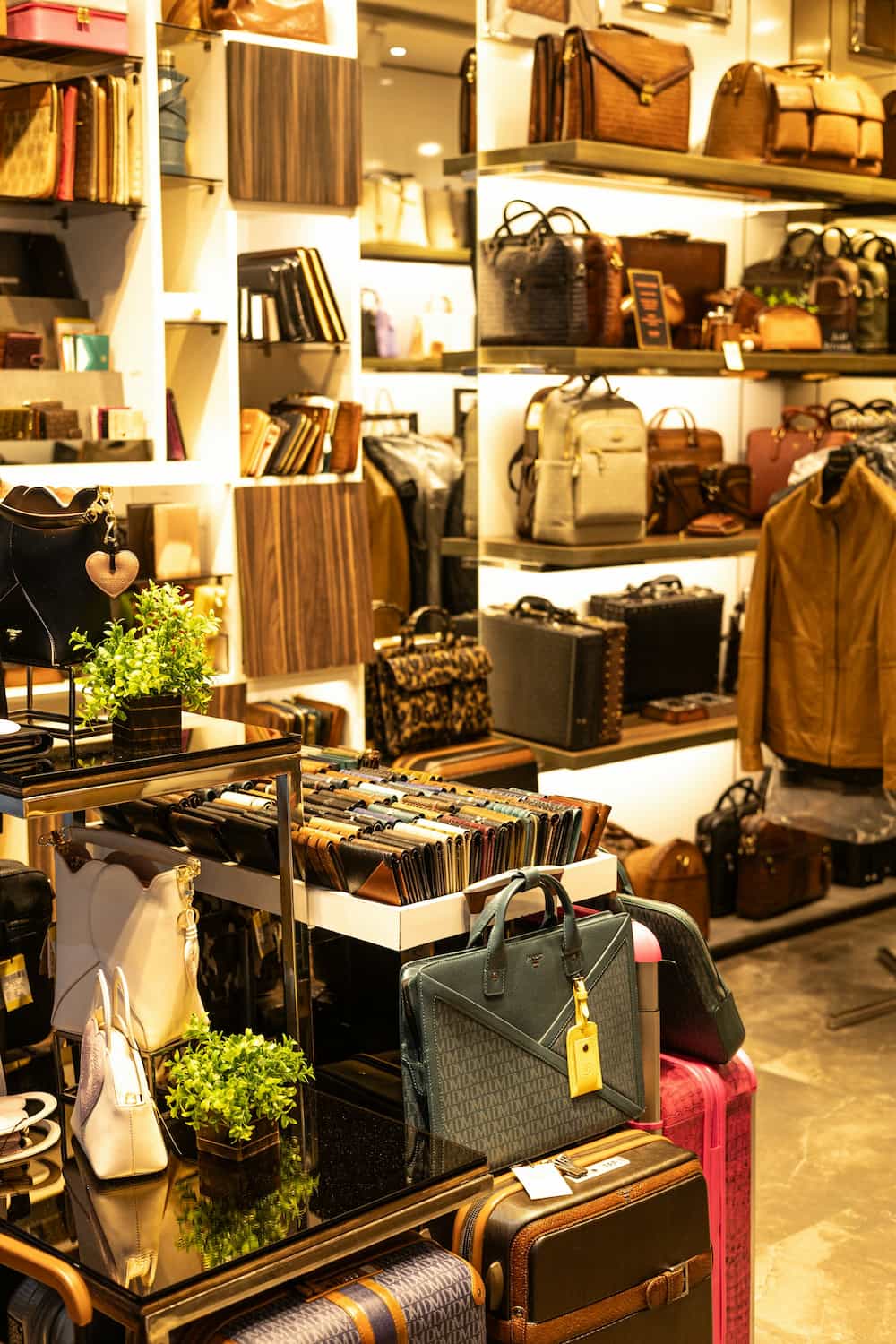 Des étagères et des tables présentent des sacs à main, des portefeuilles, des bagages et des accessoires en cuir dans un magasin de détail bien éclairé doté d'un agencement de bureau moderne qui améliore l'expérience d'achat.