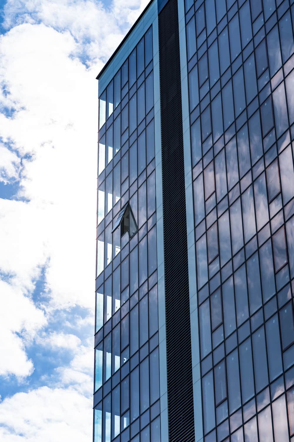 Façade en verre d'un immeuble moderne reflétant les nuages et le ciel, avec une fenêtre ouverte - une toile de fond inspirante pour un agencement de bureau innovant.