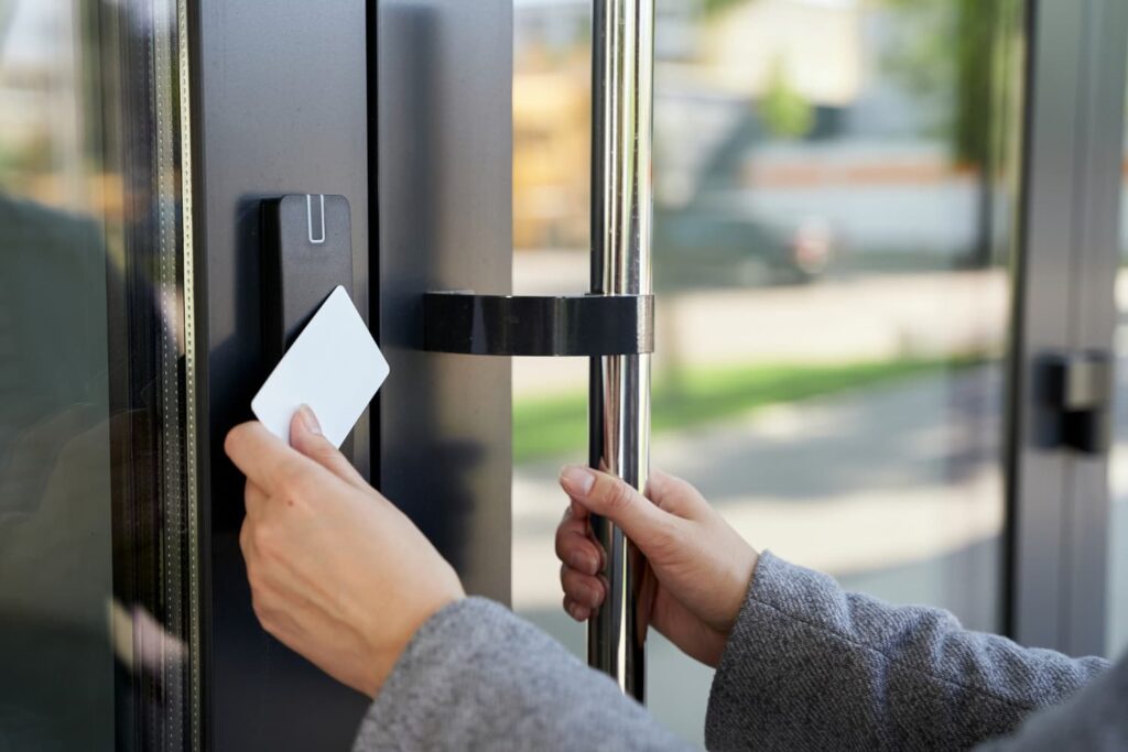 Une personne présente une carte-clé blanche à un lecteur de carte électronique, mettant en valeur la technologie moderne des réseaux électriques, tout en saisissant une poignée de porte métallique.