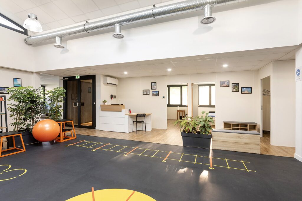 Intérieur d'un bureau ou d'une clinique moderne avec un bureau d'accueil, des plantes d'intérieur, des œuvres d'art murales, des sièges et des appareils d'exercice sur un sol noir avec des marques jaunes.