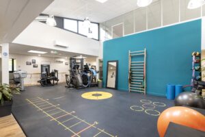 Salle de sport spacieuse équipée d'appareils d'exercice, d'un mur d'escalade, de marquages au sol, de tapis de yoga, de ballons de médecine et de grandes fenêtres laissant entrer la lumière naturelle.