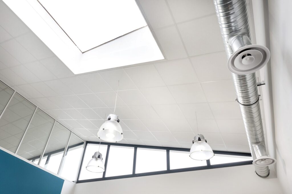 Vue du plafond d'une pièce moderne dotée d'un puits de lumière, de trois dômes suspendus, de gaines apparentes et de fenêtres près du plafond.