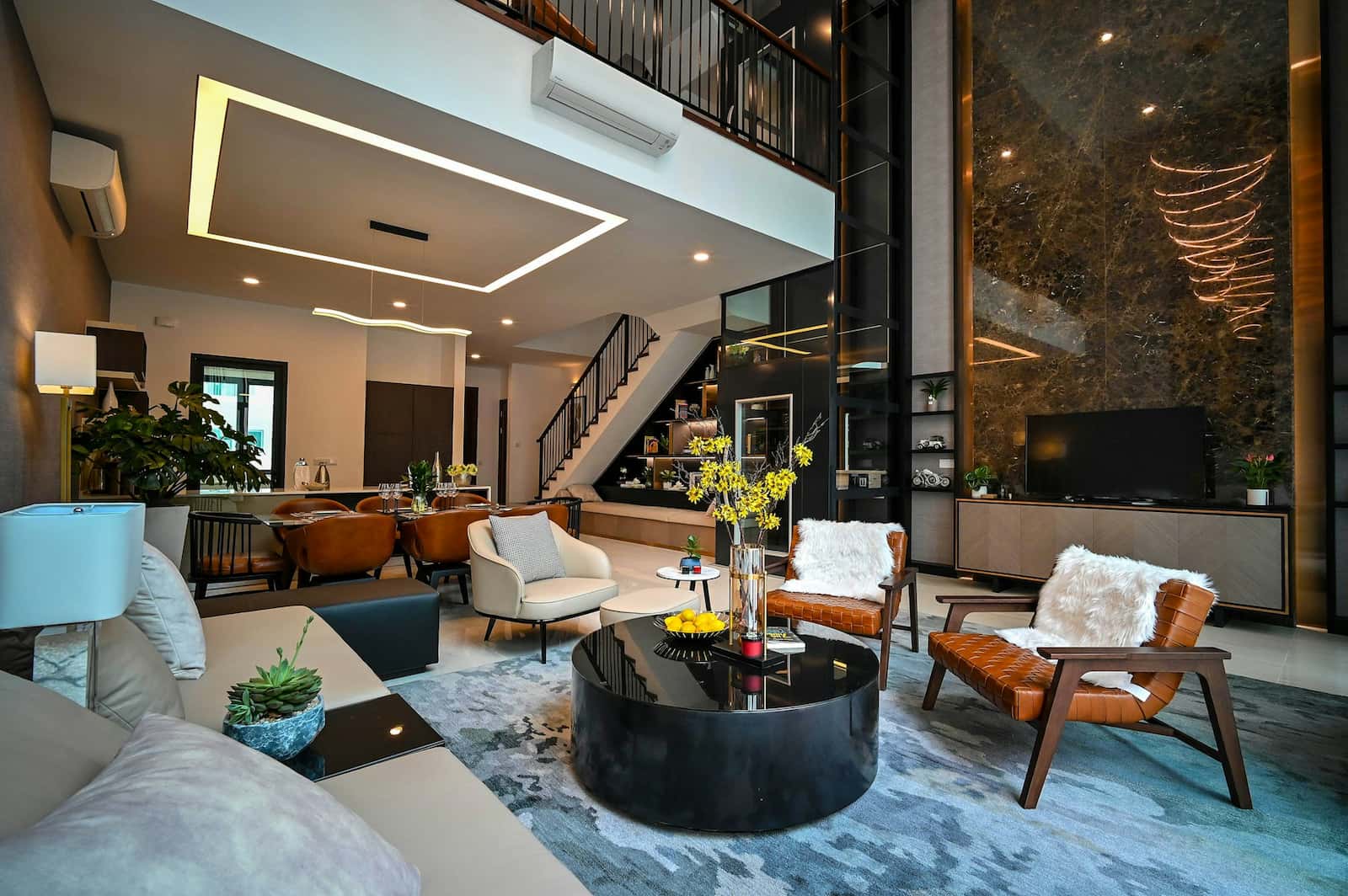 Salon moderne à aire ouverte avec mobilier contemporain, table basse en verre, plantes décoratives et escalier menant à l'étage supérieur. Tons neutres, éclairage d'appoint et grandes fenêtres.