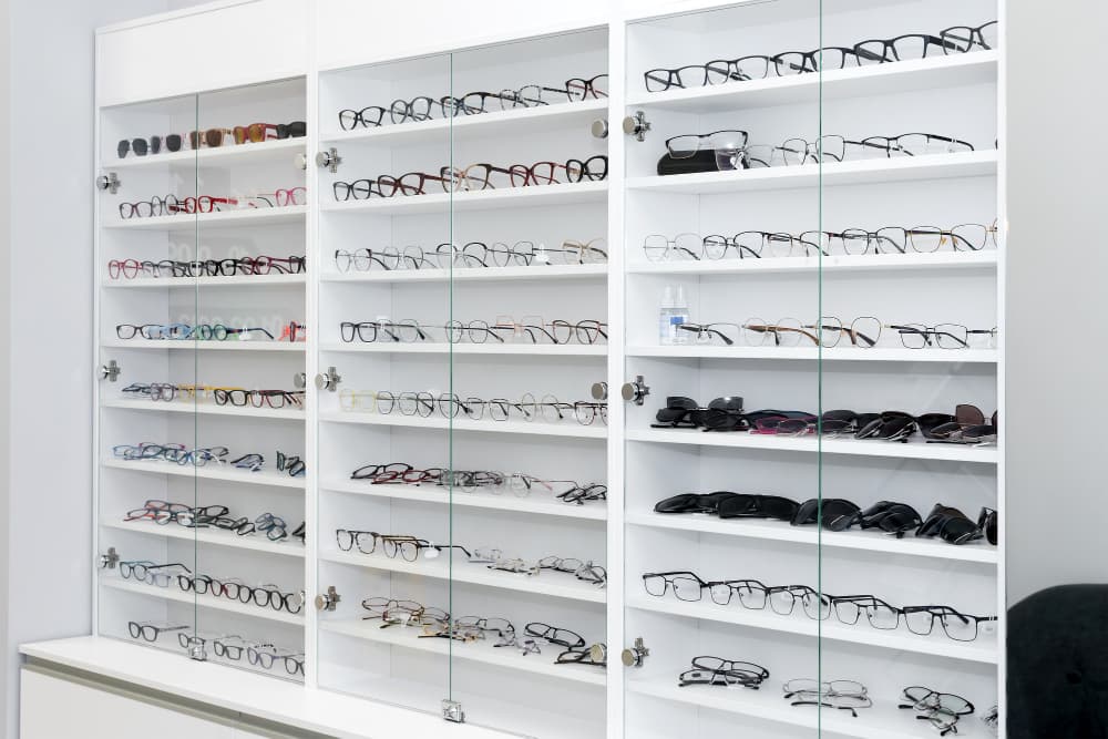 Une vitrine blanche avec des portes en verre montrant plusieurs rangées de lunettes de vue et de soleil assorties, disposées proprement sur des étagères.