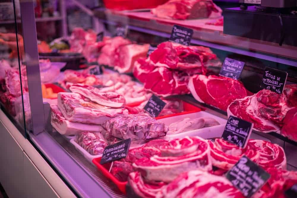 Différents morceaux de viande crue présentés dans la vitrine d'une boucherie, avec des étiquettes identifiant chaque type de viande.