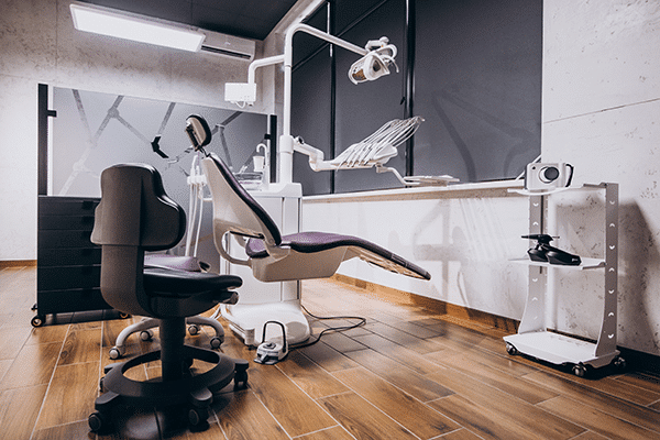 Cabinet dentaire moderne avec un fauteuil de dentiste vide, un équipement, un plafonnier et des tabourets roulants sur un sol en bois.