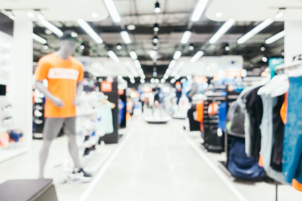Image floue de l'intérieur d'un magasin de vêtements avec des mannequins, des étagères de vêtements et un éclairage lumineux.
