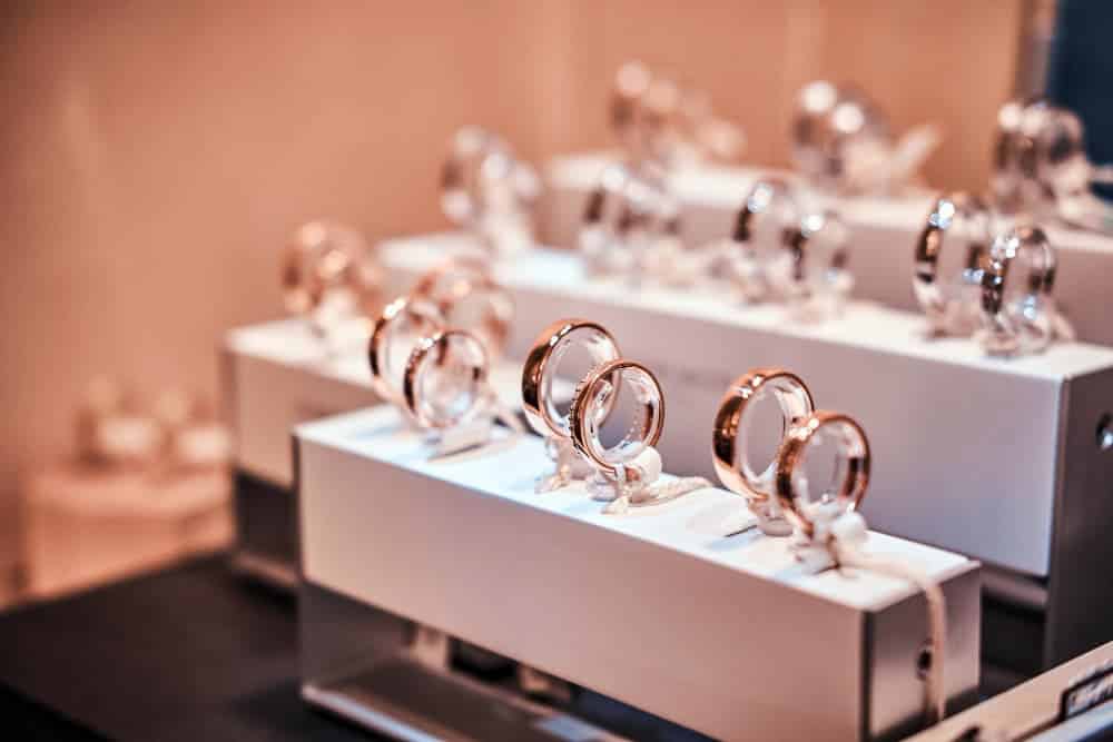 Plusieurs bagues en or et en argent sont exposées sur des présentoirs blancs dans une bijouterie.