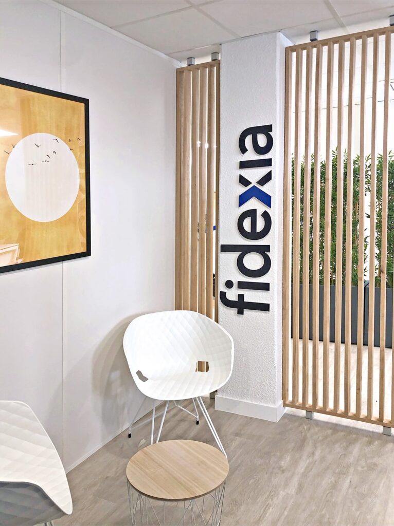 Un pilier blanc texturé avec le logo "fidexia" et des lattes de bois verticales.