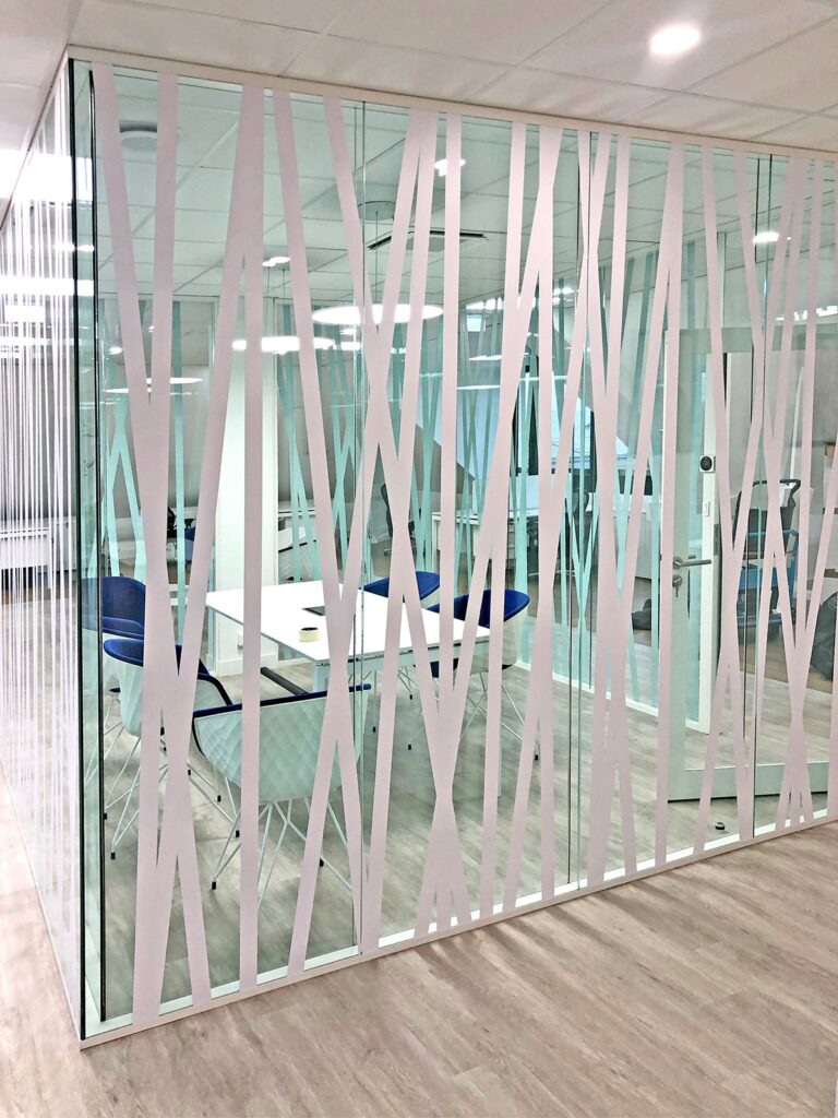 Salle de réunion de bureau vitrée avec des motifs croisés blancs, une table blanche, des chaises bleues et un sol d'aspect bois, vue de l'extérieur de la salle.