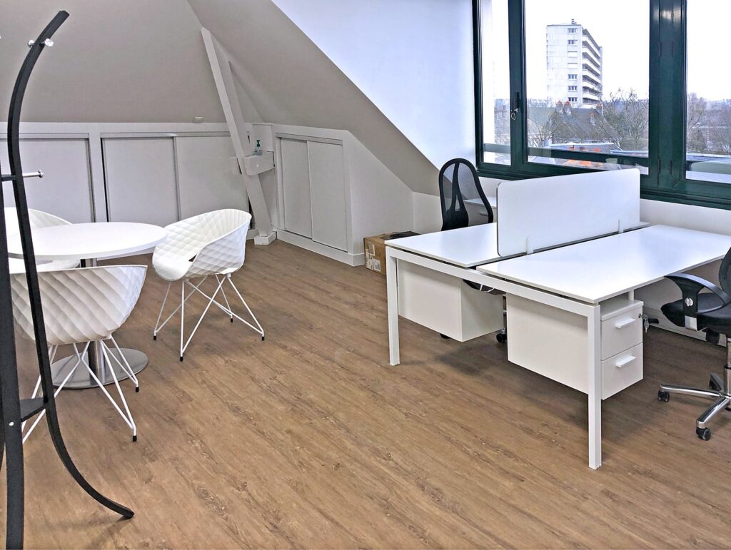 Bureau moderne avec deux bureaux blancs, deux chaises de bureau, une table ronde avec trois chaises, un sol en bois et de grandes fenêtres donnant sur les bâtiments de la ville.