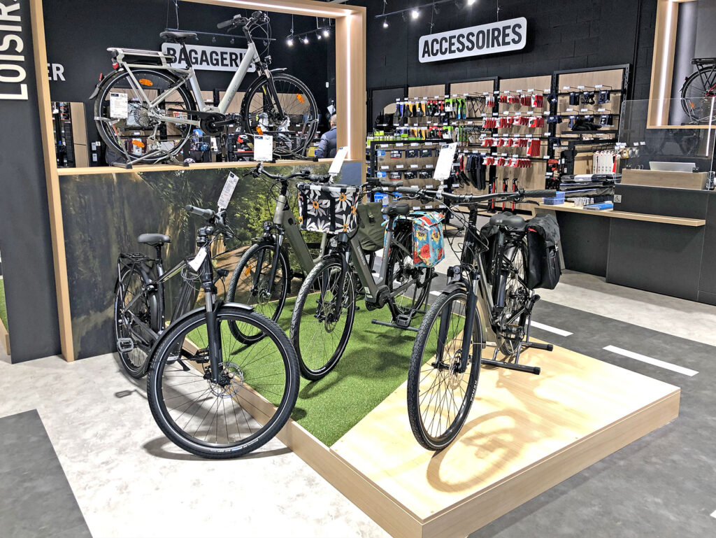 Présentation de vélos et d'accessoires de cyclisme dans un magasin, avec des vélos disposés sur une plate-forme surélevée et des étagères d'accessoires à l'arrière-plan.
