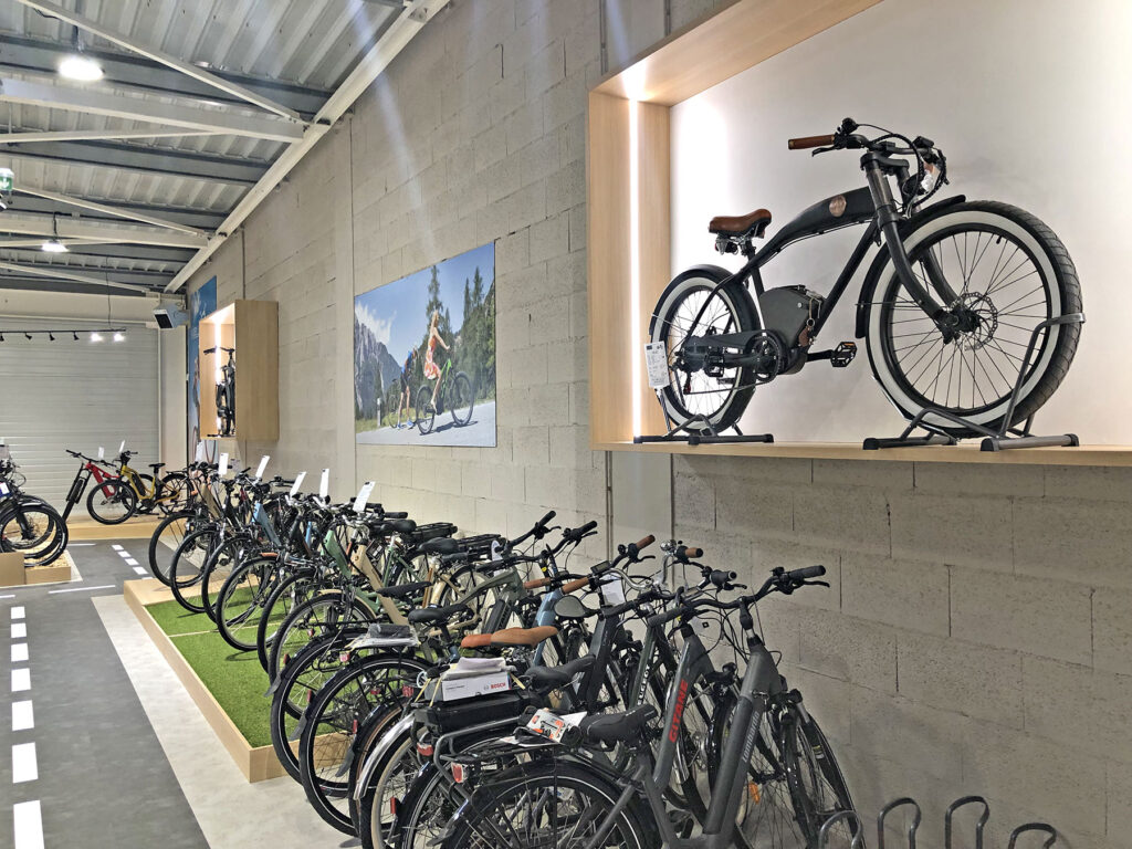 Une rangée de bicyclettes est exposée dans une salle d'exposition, une bicyclette étant présentée sur une étagère en bois au-dessus des autres, contre un mur de briques grises.
