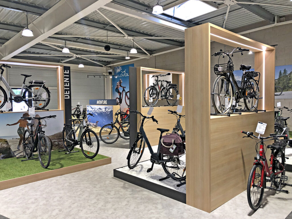 Une salle d'exposition de bicyclettes avec différents vélos exposés sur des supports et des plates-formes, un éclairage moderne et des affiches sur le cyclisme sur les murs.