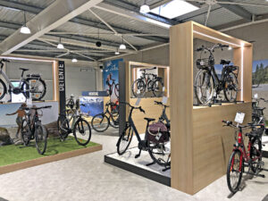 Une salle d'exposition de bicyclettes avec différents vélos exposés sur des supports et des plates-formes, un éclairage moderne et des affiches sur le cyclisme sur les murs.