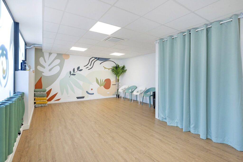 Une pièce moderne et lumineuse avec un sol en bois, des rideaux vert pâle, des chaises sarcelles et une fresque abstraite colorée sur le mur.