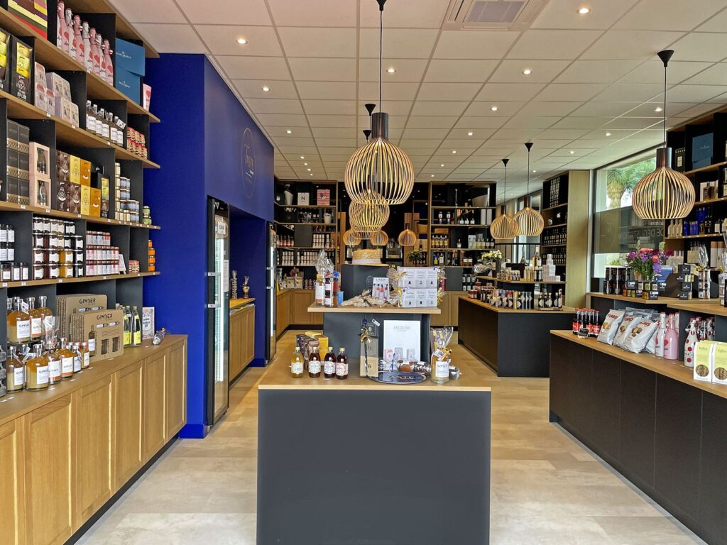 Magasin moderne de produits alimentaires et de boissons avec des étagères en bois, des produits bien rangés, des lampes suspendues et une table d'exposition centrale.