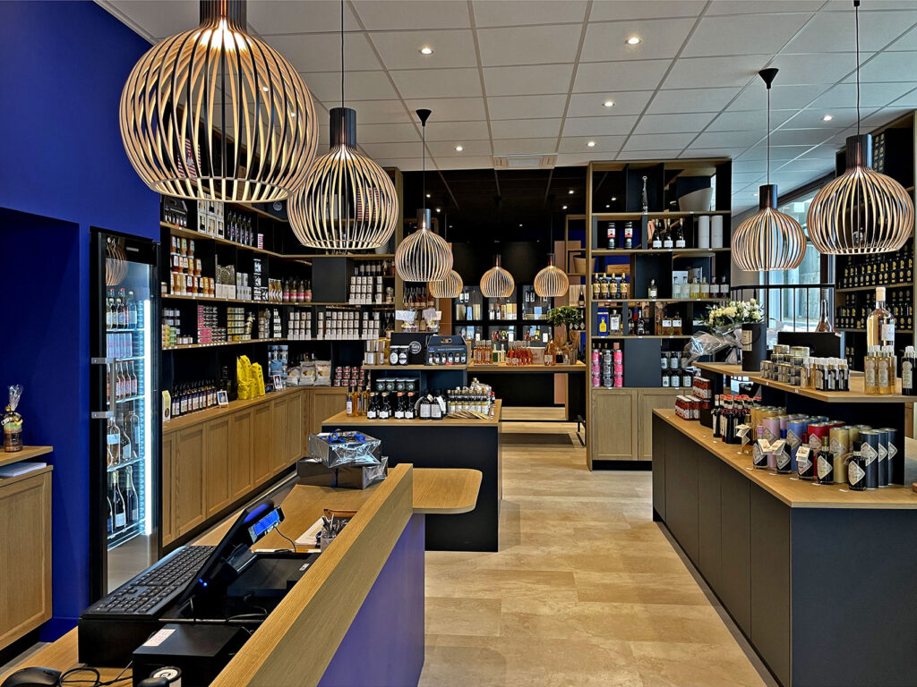 Vue intérieure d'un magasin de détail bien éclairé dont les étagères sont remplies de bouteilles et de bocaux. Plusieurs grandes lampes suspendues à lamelles sont accrochées au plafond.