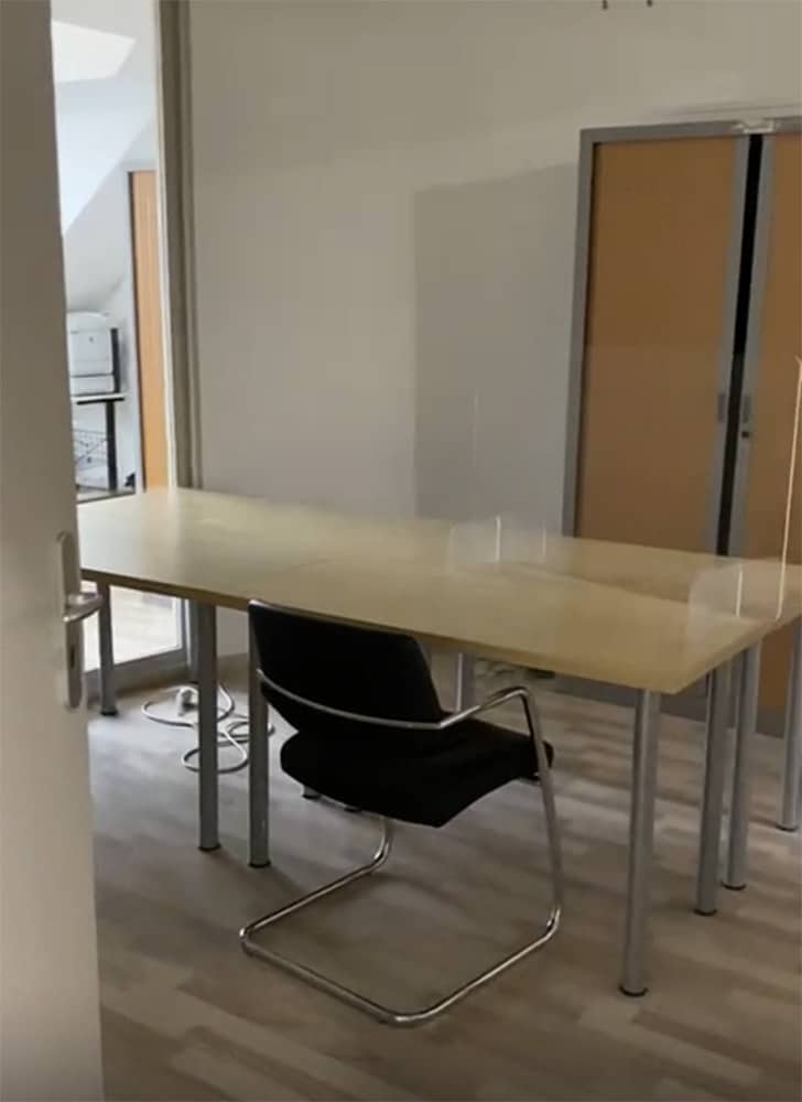 Une longue table avec une chaise et des séparateurs transparents est présentée dans un bureau.