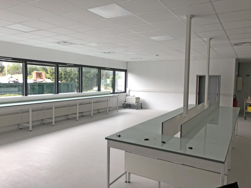 Un laboratoire spacieux et vide avec des murs blancs, de grandes fenêtres, de longues tables de travail et des plafonniers.