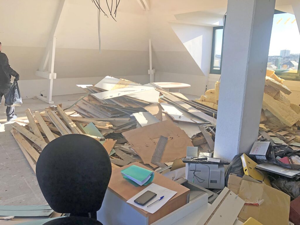 Un bureau en cours de rénovation avec des débris et des matériaux de construction éparpillés sur le sol ; un bureau avec des papiers et une chaise au premier plan.