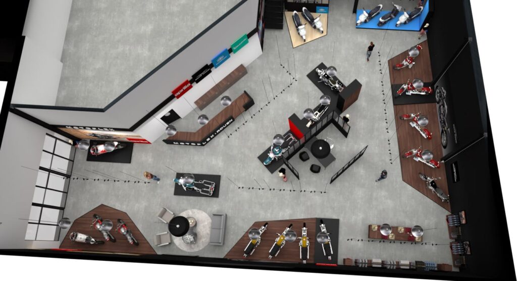 Vue de haut en bas d'une salle d'exposition moderne présentant plusieurs motos, des tables, des chaises et quelques personnes marchant dans des allées désignées.