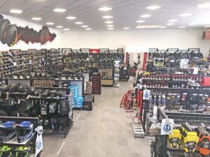 Un grand magasin d'équipement et d'accessoires pour motocycles avec des casques, des sacs à dos, des huiles et divers équipements bien rangés sur des étagères et des rayonnages.