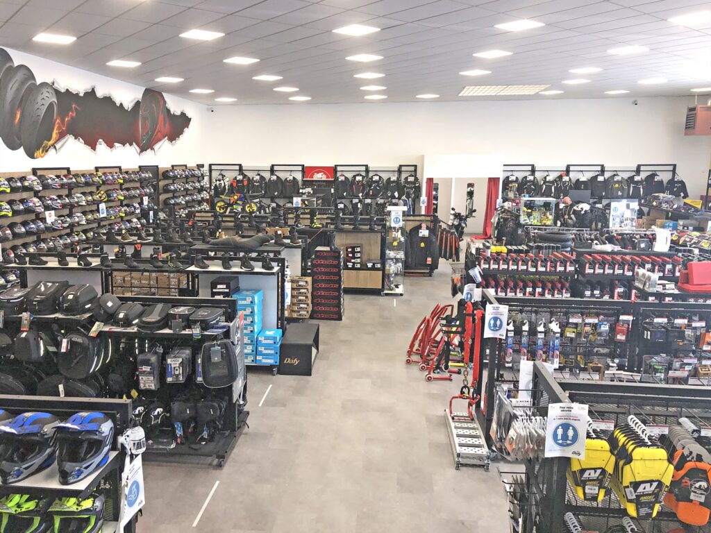 Intérieur d'un magasin d'équipement et d'accessoires pour motocyclistes, avec des casques, des vestes, des gants et de l'équipement soigneusement présentés sur des étagères et des rayonnages.