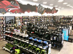 L'intérieur d'un magasin de matériel de moto présente des rangées de casques, d'accessoires et d'équipements, avec une peinture murale représentant des roues de moto sur le mur au-dessus des étagères.