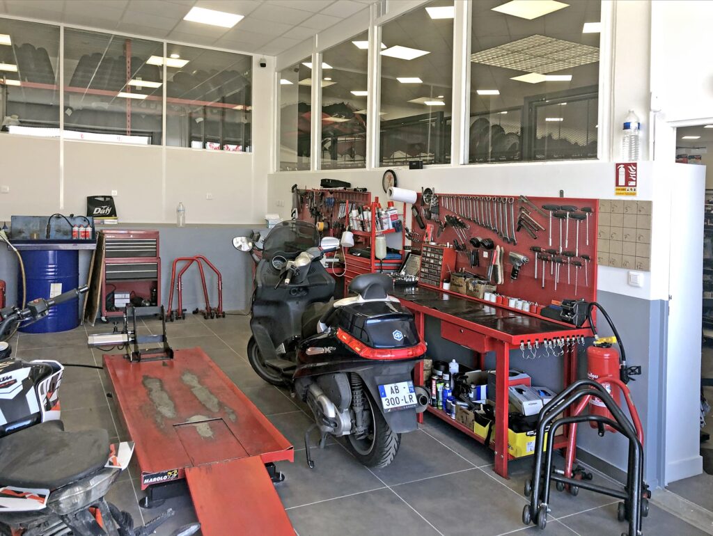Intérieur d'un atelier de réparation de motos avec des outils, un scooter et des pièces détachées.