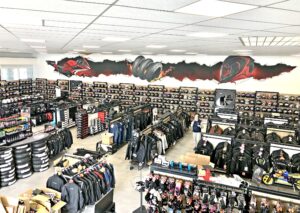 Un magasin d'équipement pour motards avec des étagères présentant des casques, des vestes et des accessoires ; des œuvres d'art murales représentant des graphiques sur le thème de la moto décorent le mur supérieur.