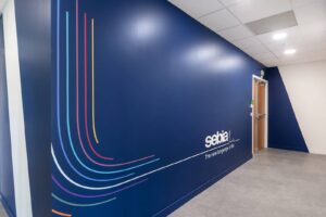 Un couloir moderne avec un mur bleu profond, des lignes courbes colorées et le logo Sebia à côté d'une porte en bois.