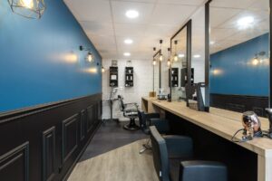 Intérieur d'un salon de coiffure moderne avec des murs bleus et noirs, des miroirs, des étagères et des fauteuils de coiffure disposés le long d'un comptoir en bois.