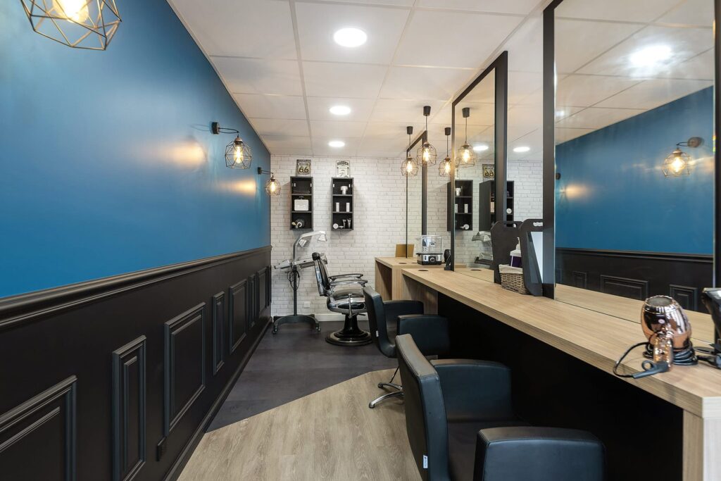 Intérieur d'un salon de coiffure avec des murs bleus et noirs, des briques blanches, un comptoir en bois avec des miroirs et des fauteuils de coiffeur noirs.