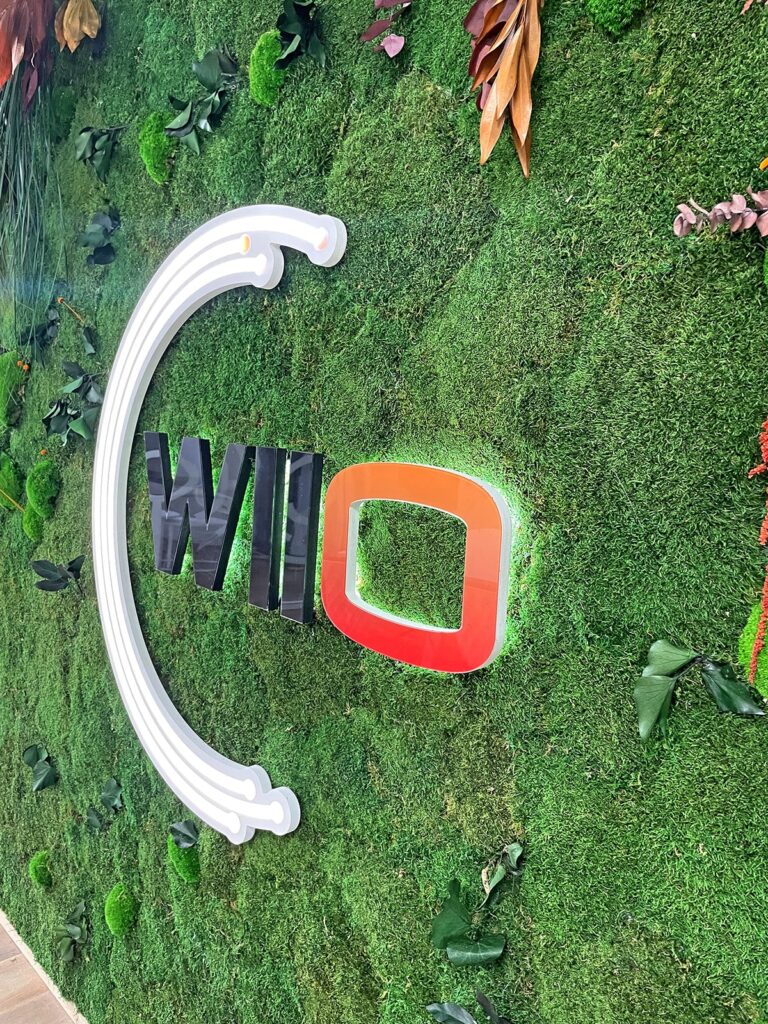 Un mur recouvert d'un gazon artificiel vert, avec le mot "Wilo" et un grand symbole blanc de parenthèse, tous deux montés sur la surface.