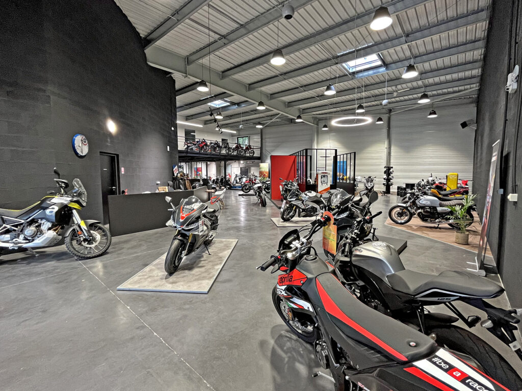 Une salle d'exposition de motos moderne avec plusieurs motos exposées au sol et une mezzanine contenant d'autres motos.