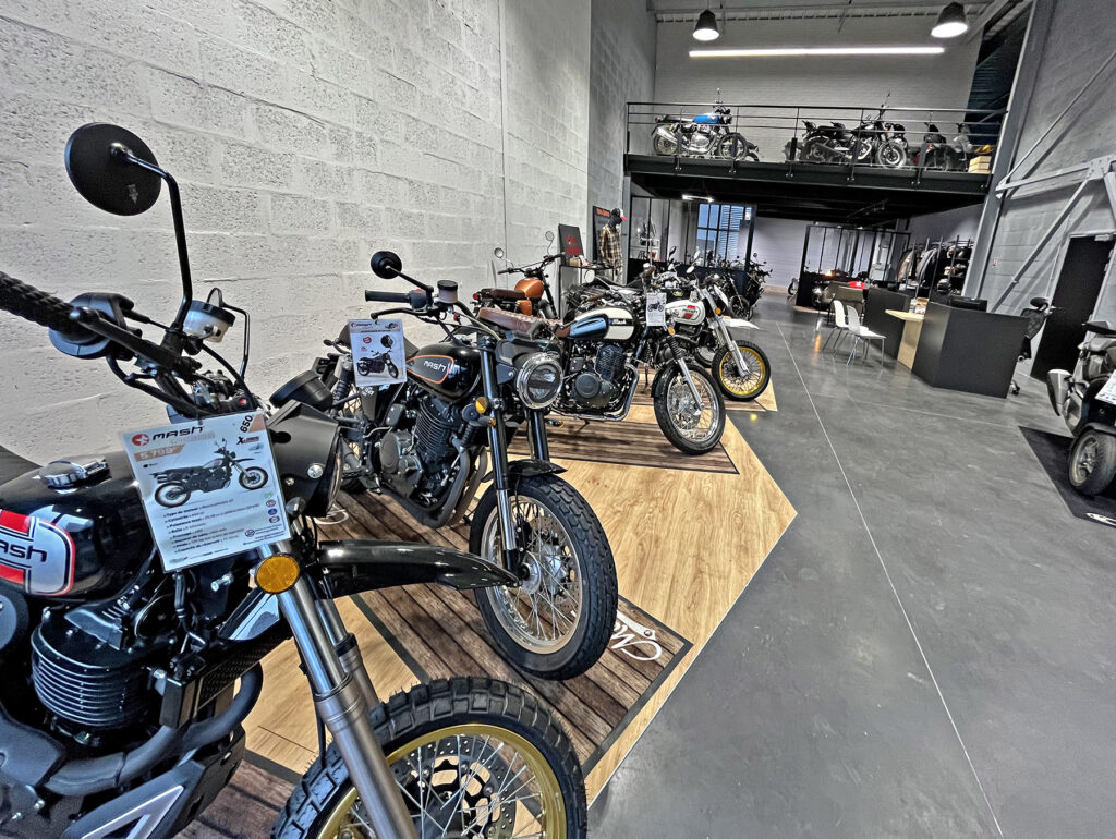 Une salle d'exposition avec plusieurs motos présentées en rang sur des plates-formes en bois, avec d'autres motos visibles sur une mezzanine à l'arrière-plan.