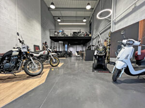 Une salle d'exposition avec des motos, un scooter et un VTT exposés ; une mezzanine située au-dessus contient d'autres motos. L'espace est doté d'un éclairage moderne et d'un intérieur industriel.