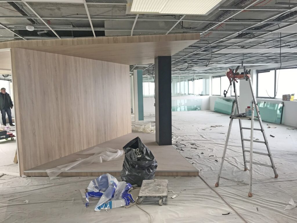 Intérieur de bureau en construction avec un mur en bois, un plafond apparent et des matériaux de construction.