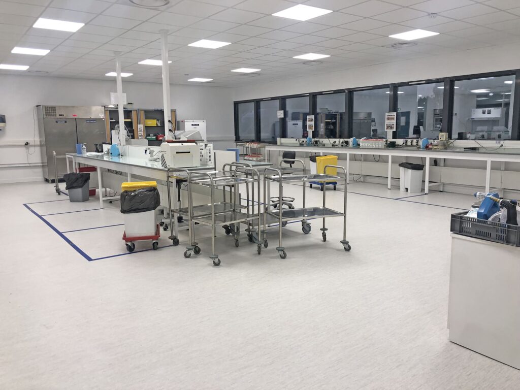 Un laboratoire propre et moderne équipé de matériel, de chariots, de poubelles et de postes de travail, bénéficiant d'un bon éclairage et de grandes fenêtres le long d'un mur.