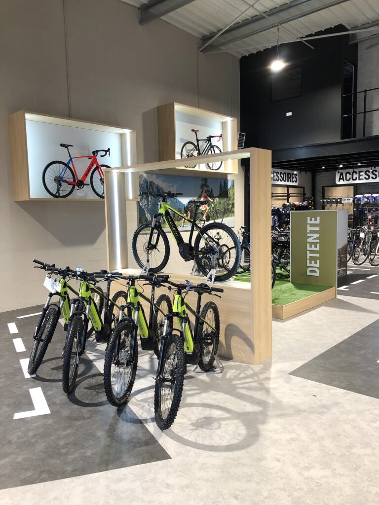 Exposition de plusieurs VTT dans une salle d'exposition bien éclairée, avec certains vélos fixés aux murs et d'autres disposés sur le sol devant un panneau "DETENTE".