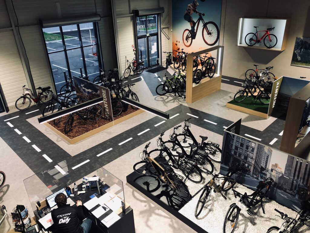 Une salle d'exposition avec plusieurs présentoirs à vélos, des vélos accrochés aux murs et une personne travaillant à un bureau près d'accessoires pour vélos.
