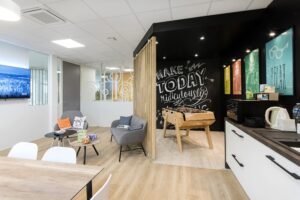 Salle de pause d'un bureau moderne avec des chaises longues, un baby-foot, une kitchenette, des œuvres d'art murales et des snacks sur une table.