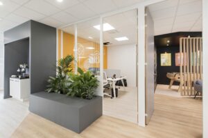 Espace de bureau moderne avec salle de réunion vitrée, plantes d'intérieur, baby-foot, parquet en bois clair et mobilier contemporain.