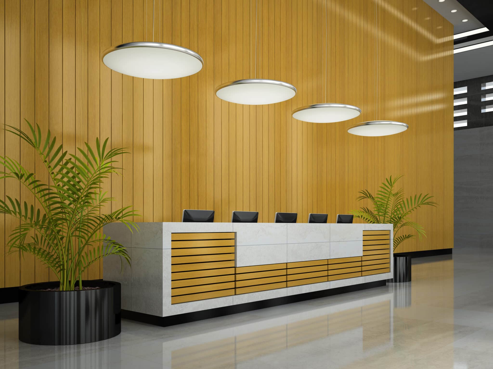Un long comptoir d'accueil dans un hall d'entrée moderne, avec un mur lambrissé de bois clair, quatre suspensions circulaires et des plantes en pot de chaque côté.