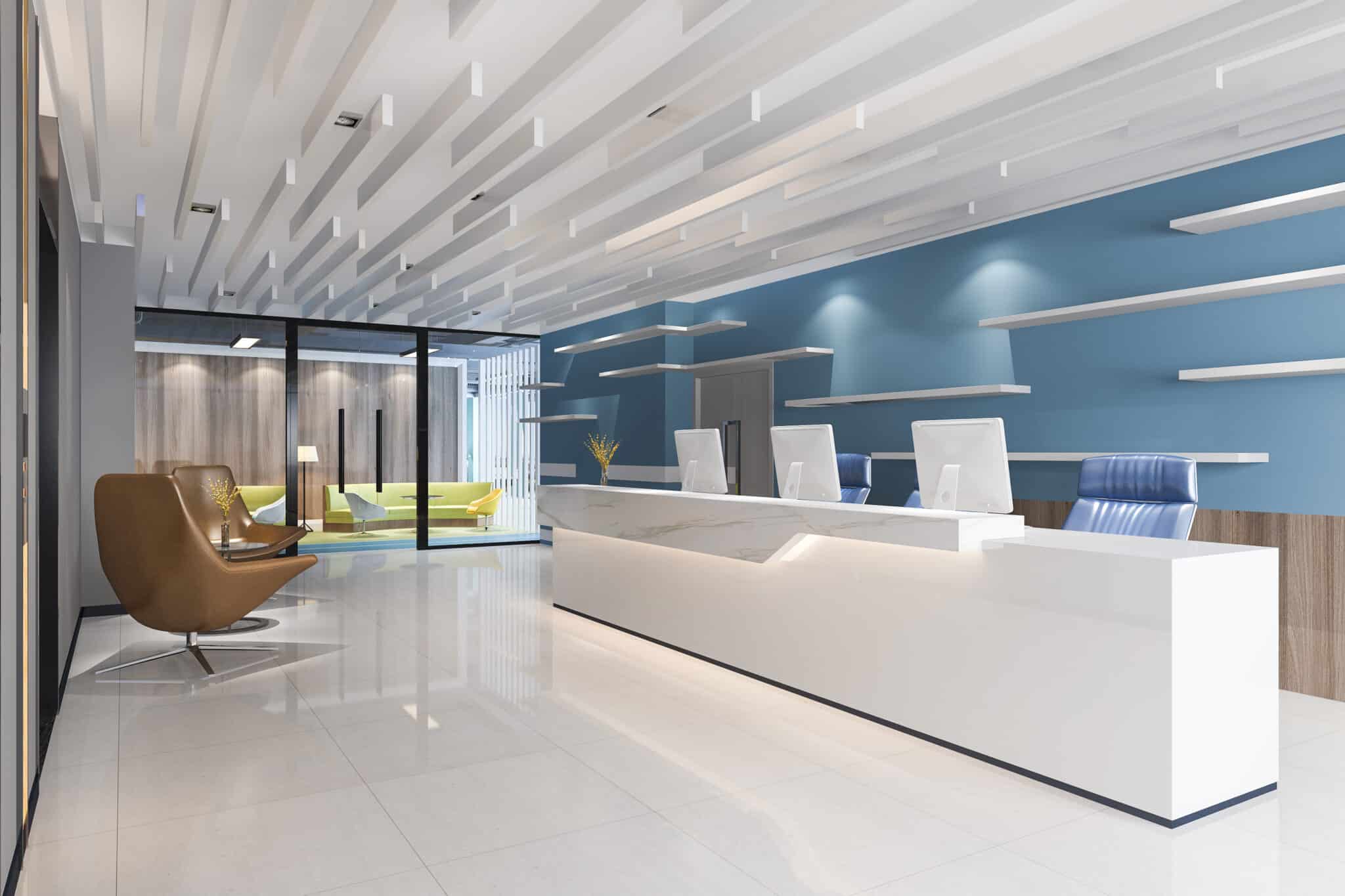 Espace d'accueil moderne avec un bureau blanc, des chaises bleues, des étagères murales et un mur d'accent bleu ; un fauteuil marron et un canapé jaune sont visibles à l'arrière-plan.
