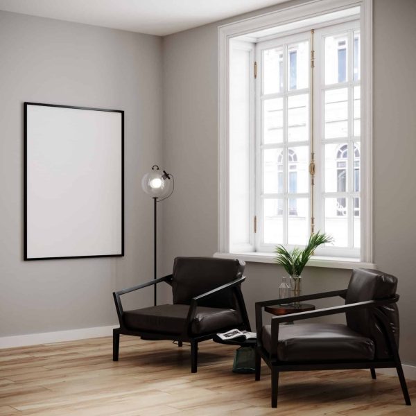 Deux fauteuils noirs et une petite table sont disposés près d'une fenêtre dans une pièce moderne dotée d'un parquet clair, d'un lampadaire et d'un cadre photo vide accroché au mur.