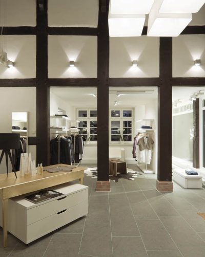 Intérieur d'une boutique de vêtements moderne avec des tons neutres, des étagères bien organisées, une table en bois clair avec des tiroirs, et de grandes fenêtres qui laissent passer la lumière naturelle.