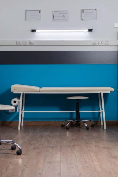 Une salle d'examen médical propre et moderne avec des couleurs bleu et blanc, une table d'examen, des chaises de bureau, des armoires et des étagères avec des classeurs.